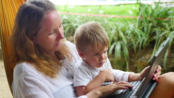 Dziewczyna i dziecko pracuje na laptopie i smartphone leżącego w hamaku — Wideo stockowe