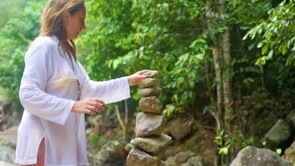 Una chica hace una escultura de equilibrio de rocas. deportes al aire libre — Vídeo de stock