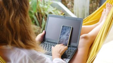 dizüstü bilgisayar ve bir hamakta yatan smartphone üzerinde çalışan kız