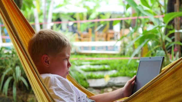 Молодой парень играет на ноутбуке, лежа в гамаке — стоковое видео