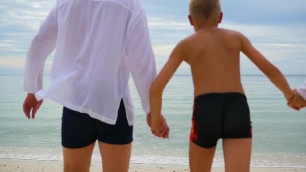 Gelukkige familie hand in hand loopt langs de kust. Om uit te voeren in het water plonsen maken — Stockvideo