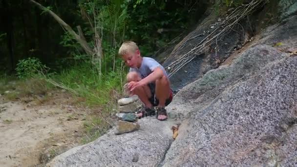 Een jonge jongen maakt een sculptuur van balans stenen. Outdoor sporten — Stockvideo