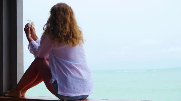La chica se sienta en la terraza y mira hacia el mar — Vídeos de Stock