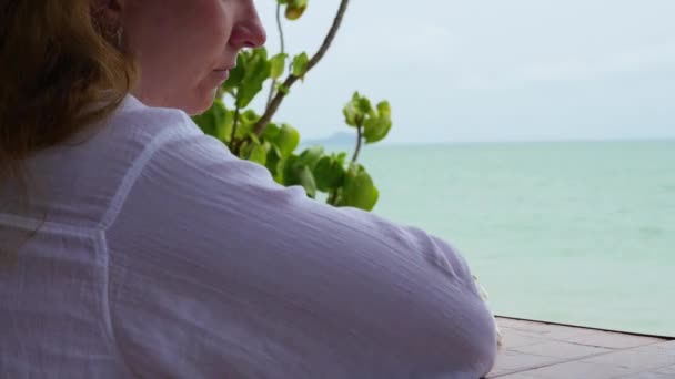 Das Mädchen sitzt auf der Terrasse und blickt zum Meer — Stockvideo