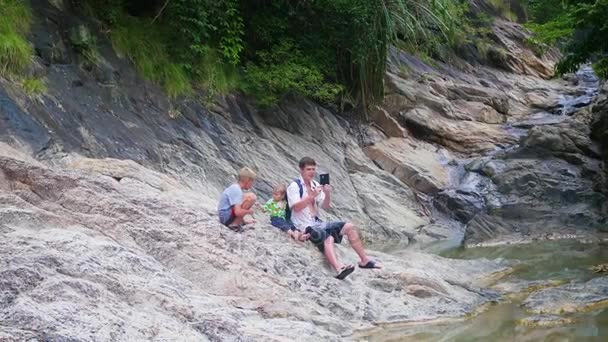 La familia se sienta en la orilla de un río de montaña. hace una foto en un smartphone — Vídeo de stock