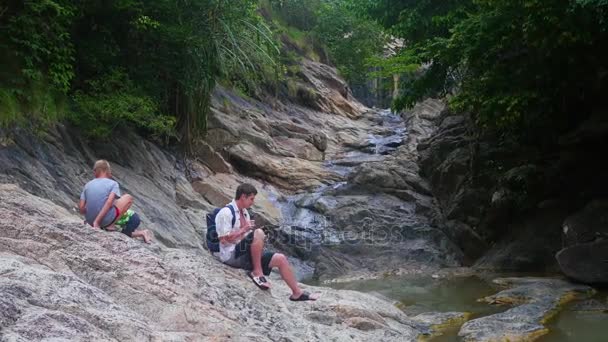 La familia se sienta en la orilla de un río de montaña. hace una foto en un smartphone — Vídeos de Stock