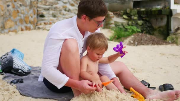Молодий чоловік грає з дитиною на пляжі. Щоб зробити піщані форми — стокове відео
