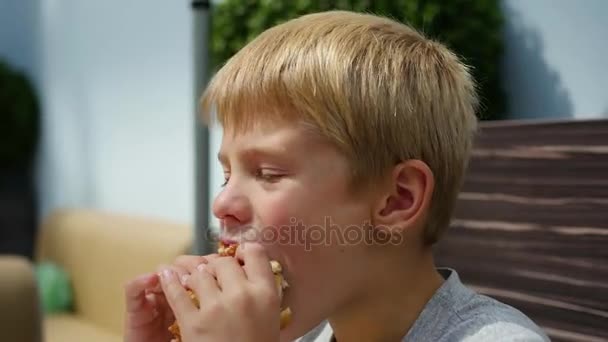 Дитина їсть булочку з котлетом і сиром у ресторані швидкого харчування — стокове відео