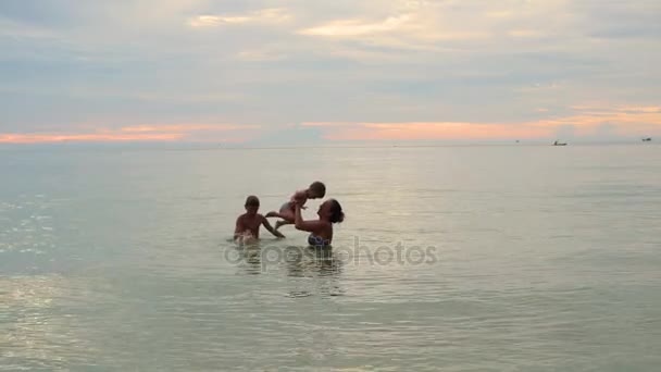 Το κορίτσι και τα παιδιά κολυμπούν και παίζουν στη θάλασσα. Ηλιοβασίλεμα ώρα — Αρχείο Βίντεο