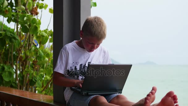 Um jovem a brincar num portátil, sentado no terraço. Perto do mar e da praia — Vídeo de Stock