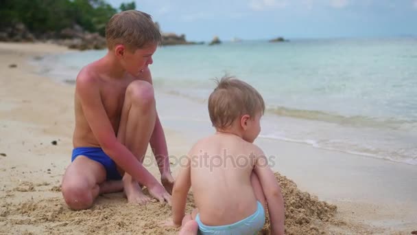 Ein junger Mann spielt mit Kind am Strand. um den Sand zu formen — Stockvideo