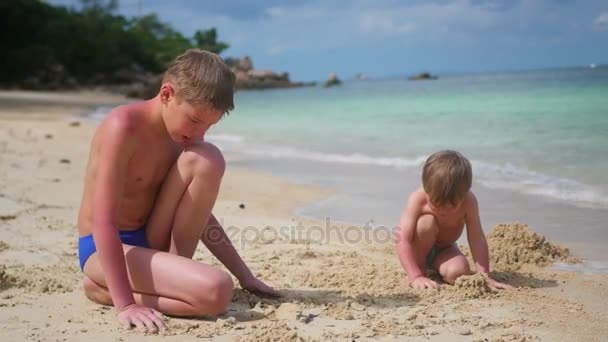 Un jeune homme joue avec un enfant sur la plage. Pour faire les moules de sable — Video