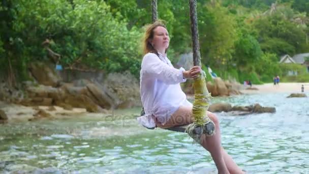 Uma menina balançando em um balanço de corda na praia — Vídeo de Stock