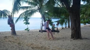 Kumsalda bir adam ve bir çocuk bir ipte sallanan salıncak. Tropik ada