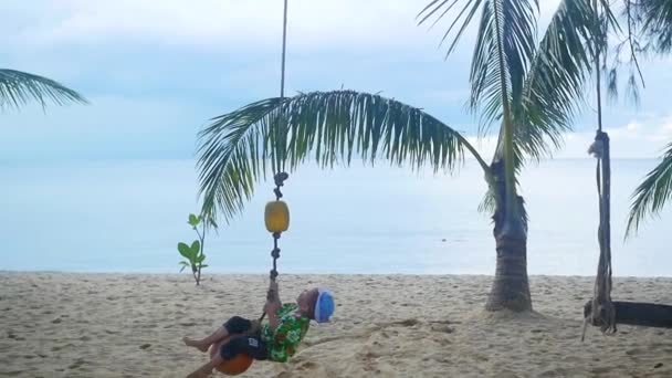 Il bambino felice che oscilla su un'altalena sulla spiaggia. Isola tropicale — Video Stock