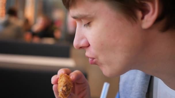 Хлопець їсть смажену курку в ресторані швидкого харчування крупним планом — стокове відео
