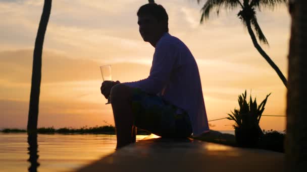 Il ragazzo seduto sulla spiaggia e bere birra.La ragazza si avvicina al ragazzo e lo abbraccia teneramente.Ora del tramonto — Video Stock