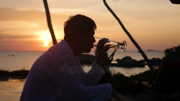 O cara sentado na praia e bebe cerveja.Hora do pôr do sol — Vídeo de Stock