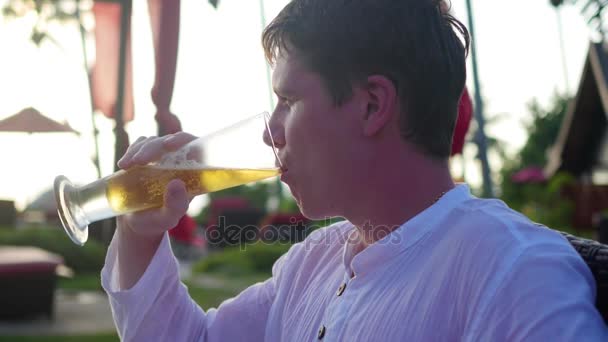 O cara sentado na praia e bebe cerveja.Hora do pôr do sol — Vídeo de Stock
