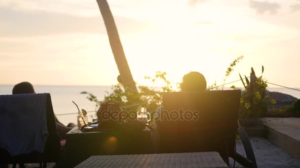 Het meisje en de jongen zitten in de ligstoelen en de zonsondergang. Tropisch eiland — Stockvideo