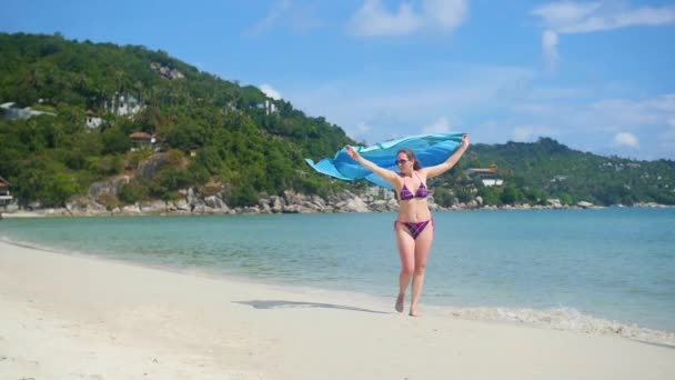 une jeune fille avec un paréo est le long du rivage de la plage. Île tropicale, le vent chaud de l'été 