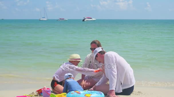 Famiglia felice con bambini che giocano sulla spiaggia di sabbia con i giocattoli. Isola tropicale, in una giornata calda — Video Stock