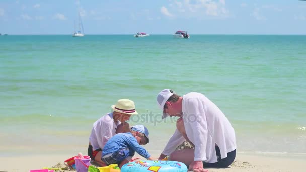 Boldog család, a gyerekek játszanak a játékokkal a homokos strandon. Trópusi sziget, egy forró napon — Stock videók