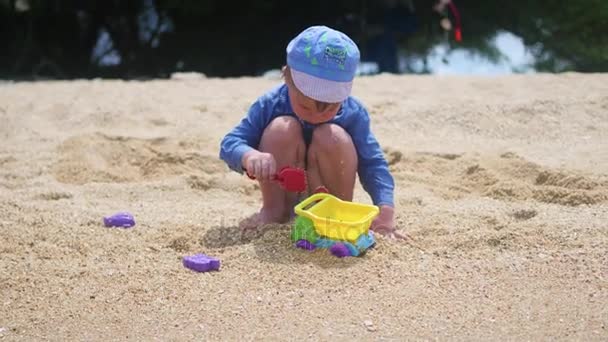 Ett barn leker med sand och leksaker på stranden en solig varm dag — Stockvideo