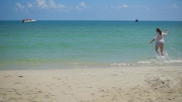 Ein junges Mädchen läuft am Strand entlang und erzeugt einen Wasserstrahl. tropische Insel, an einem heißen Tag — Stockvideo