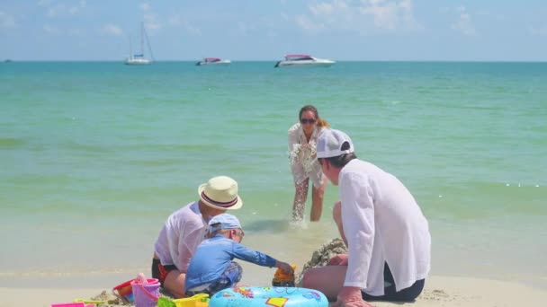 Glückliche Familie mit Kindern, die am Sandstrand mit Spielzeug spielen. tropische Insel, an einem heißen Tag — Stockvideo