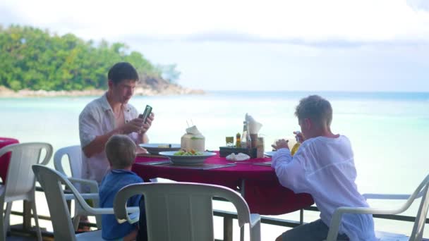Семья с детьми обедает в ресторане на пляже. продукты питания на открытом воздухе — стоковое видео