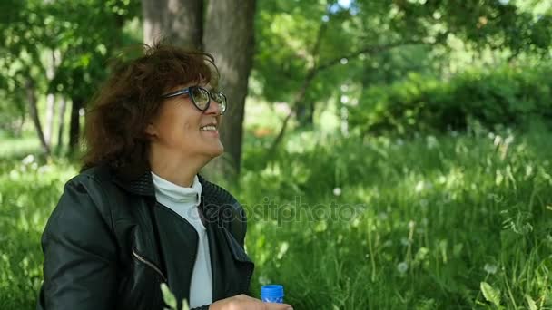 Женщина сидит на траве и улыбается. Семейный отдых в парке — стоковое видео
