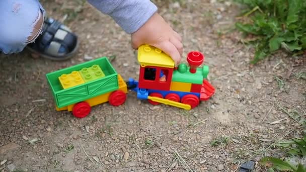 Uma criança brinca com um trem de brinquedo na areia. Jogos ao ar livre — Vídeo de Stock