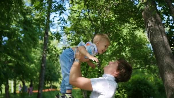 Slow-motion. een jonge vader zijn lachende baby overgeven in de lucht. Outdoor recreatie — Stockvideo