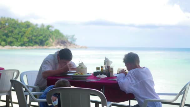 Rodina s dětmi večeří v restauraci na pláži. jídlo venku — Stock video