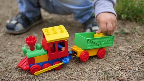 Un niño juega con un tren de juguete en la arena. Juegos al aire libre — Vídeos de Stock