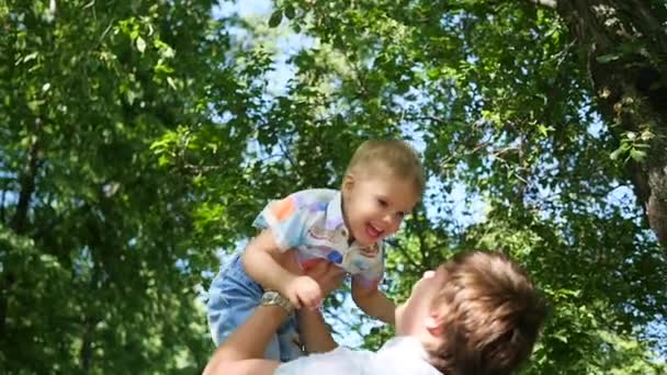 En cámara lenta. un padre joven arrojando al aire a su bebé risueño. recreación al aire libre — Vídeos de Stock