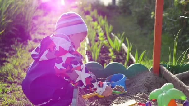 El niño juega con los juguetes en la caja de arena.Verano Día soleado. Diversión y juegos al aire libre — Vídeos de Stock