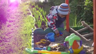 Çocuk kum havuzunda oyuncaklarla oynar. Yaz güneşli gün. Eğlence ve oyun açık havada