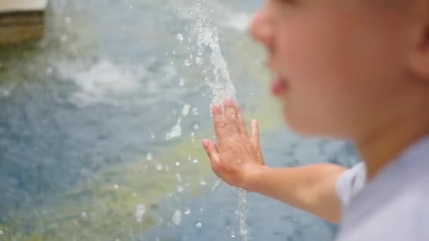 Ein Kind spielt mit Wasserstrahl im Brunnen. Sommersonniger Tag. Spiel und Spaß im Freien — Stockvideo