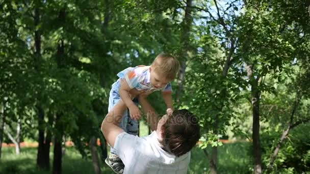 En cámara lenta. un padre joven arrojando al aire a su bebé risueño. recreación al aire libre — Vídeo de stock