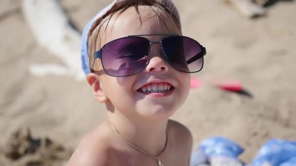 Ребенок пытается носить солнечные очки. Пляж, солнечный жаркий день — стоковое видео