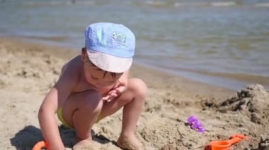 Bir çocuk kum ve oyuncaklar ile sahilde sıcak güneşli bir günde çalış