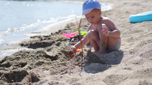 Дитина грає з піском та іграшками на пляжі в сонячний спекотний день. Розваги та ігри на відкритому повітрі — стокове відео