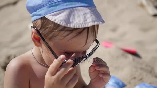 Дитина намагається носити сонцезахисні окуляри. Пляж, сонячний спекотний день — стокове відео