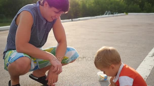 Familia con niño dibuja con tiza en el asfalto. juegos al aire libre — Vídeos de Stock