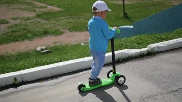 Un enfant heureux monte son scooter dans le parc. — Video