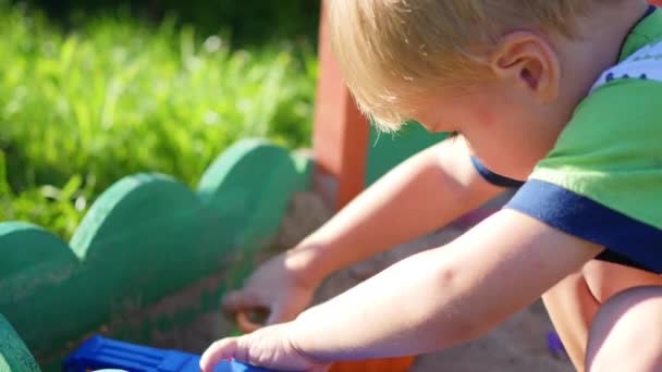 A criança brinca com os brinquedos na sandbox.Summer dia ensolarado. Diversão e jogos ao ar livre — Vídeo de Stock