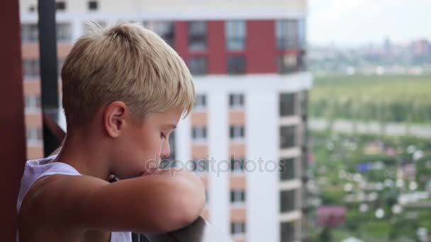 Tiener staat op het balkon van een hoog gebouw en kijkt neer — Stockvideo