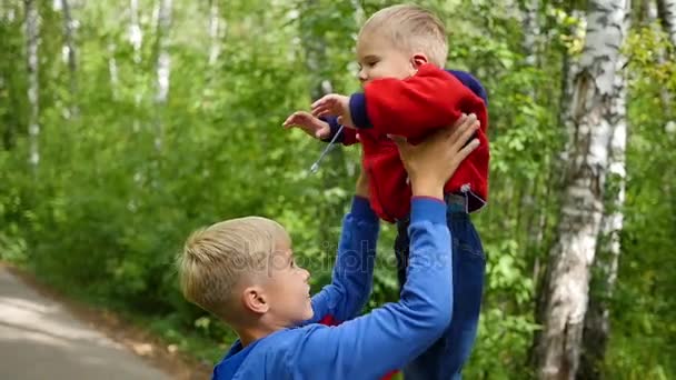 Slow motion. Det äldre barnet kastar brodern skrattande i luften. Utomhusaktiviteter — Stockvideo